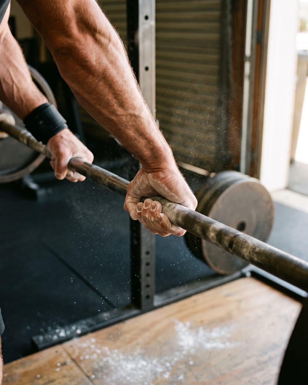 Chalked hands gripping a barbell in a small strength gym
