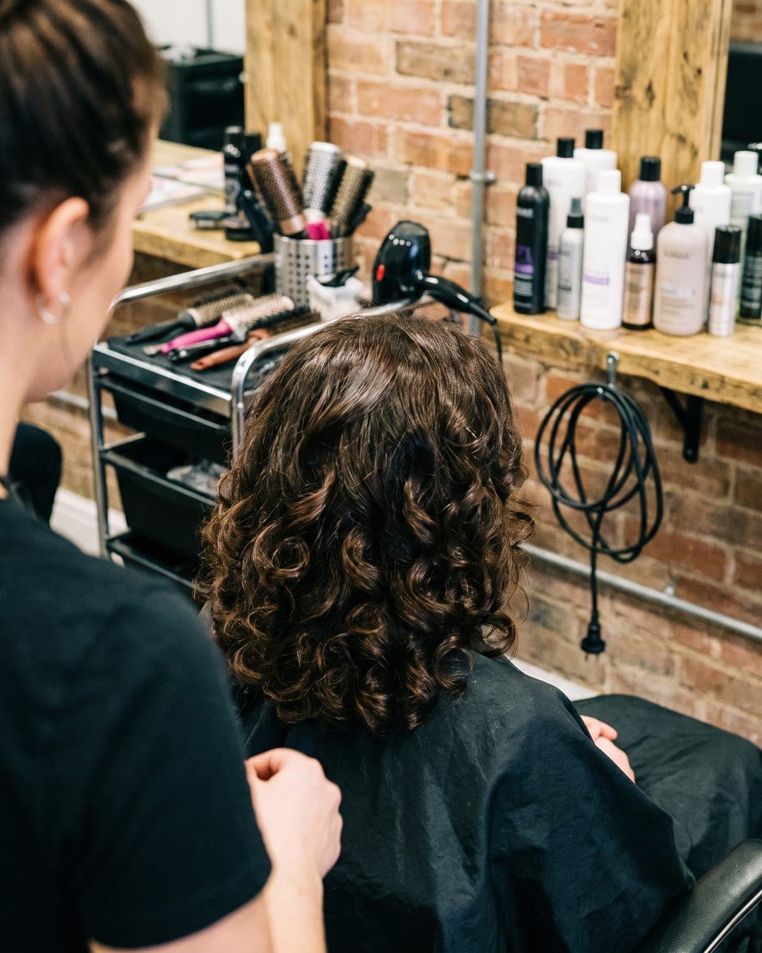 Phone photo of the back of a client’s head with fresh glossy curls in a busy salon
