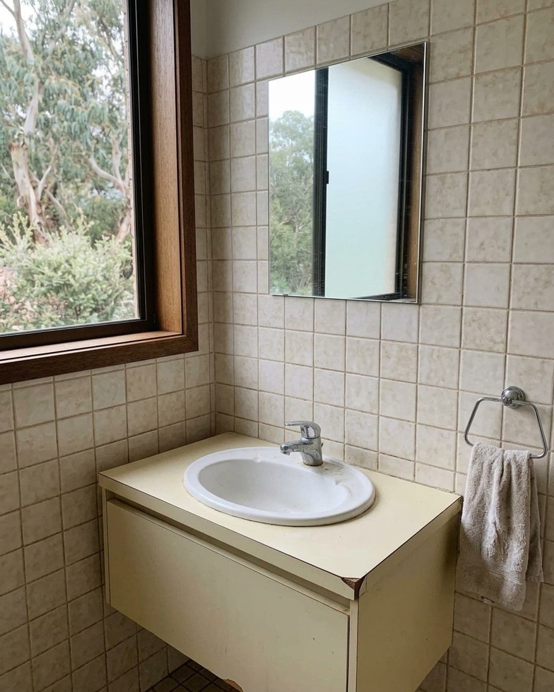 Phone photo of the same bathroom before the refit, with dated beige tiles and an old chrome tap